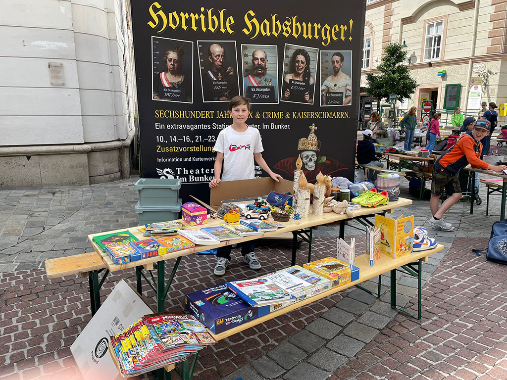 Ein Junge steht hinter einem großen Tisch mit Spielzeug, Büchern und Deko