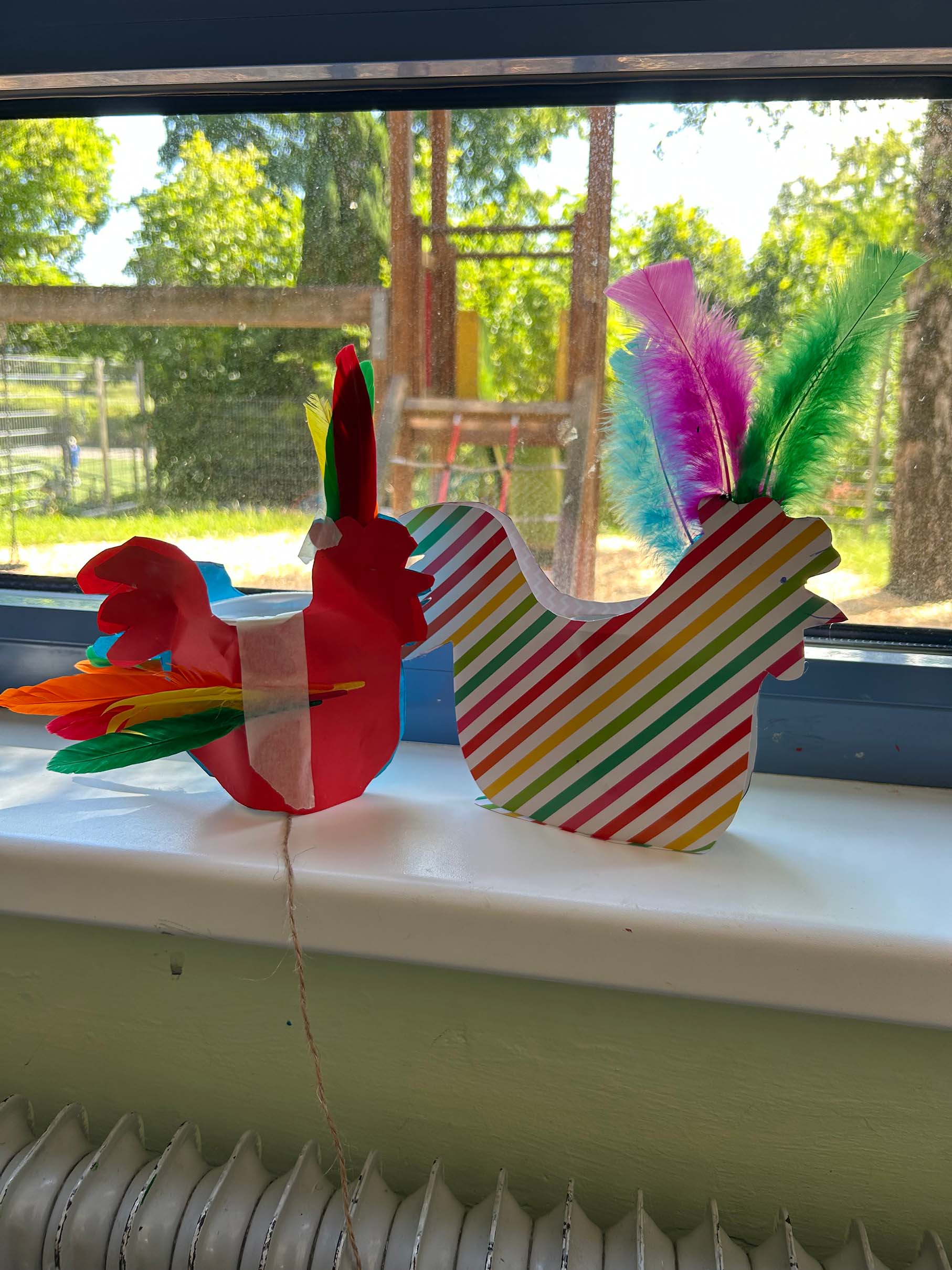 Zwei selbstgemachte Hühner aus buntem Papier stehen auf einer Fensterbank