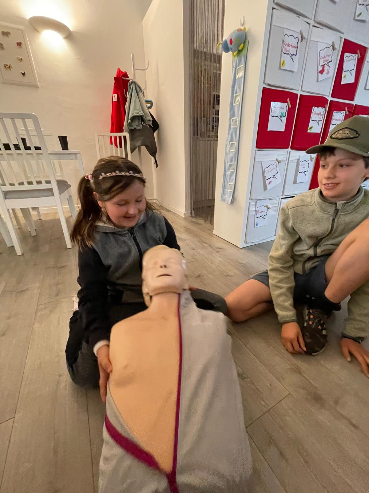 Ein Mädchen hält eine Erste-Hilfe-Puppe und ein Junge sitzt daneben.