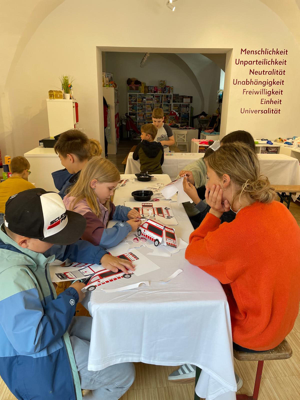 Mehrere Kinder sitzen an einem Tisch und basteln einen Rettungswagen.