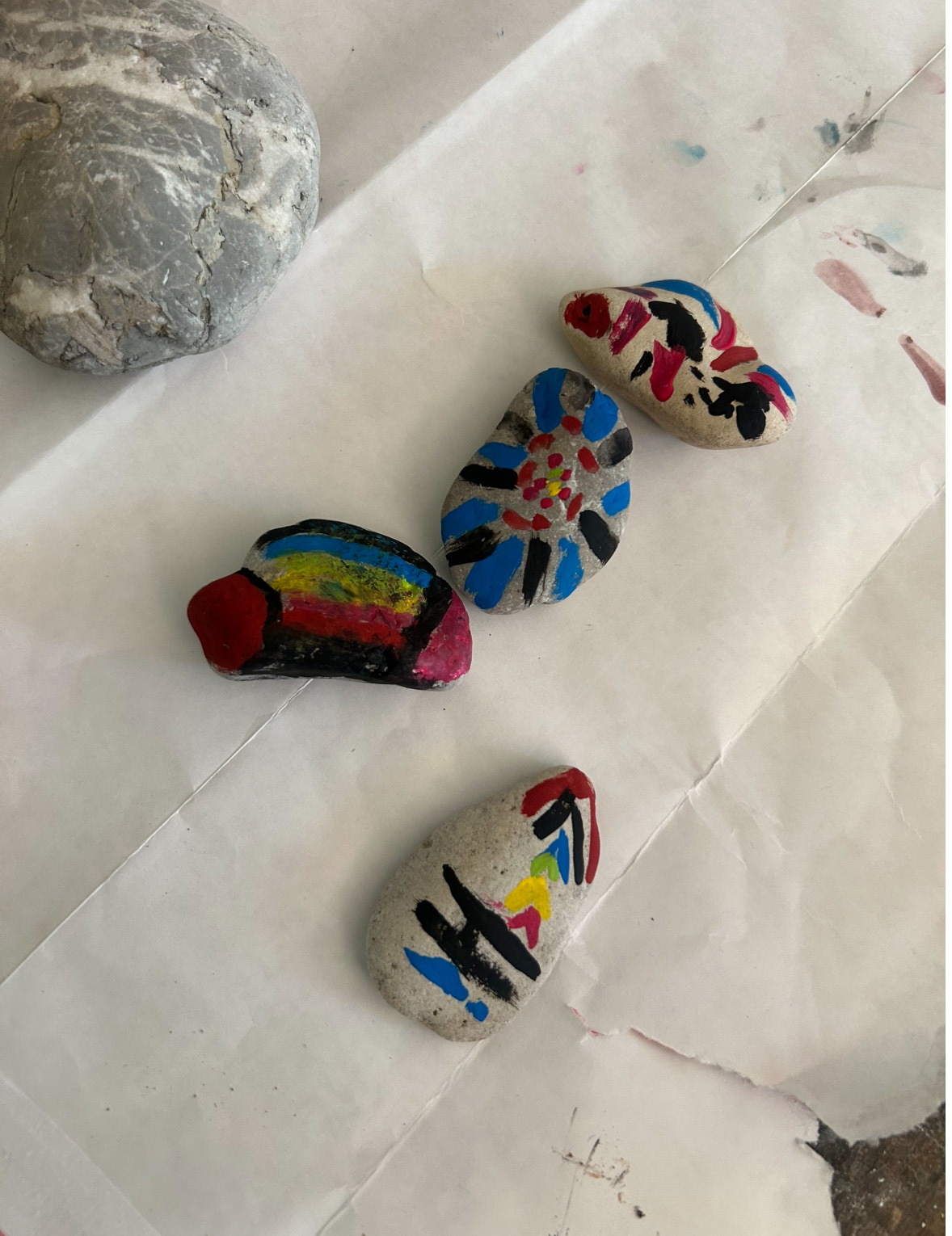 4 bunt bemalte Steine liegen auf Papier