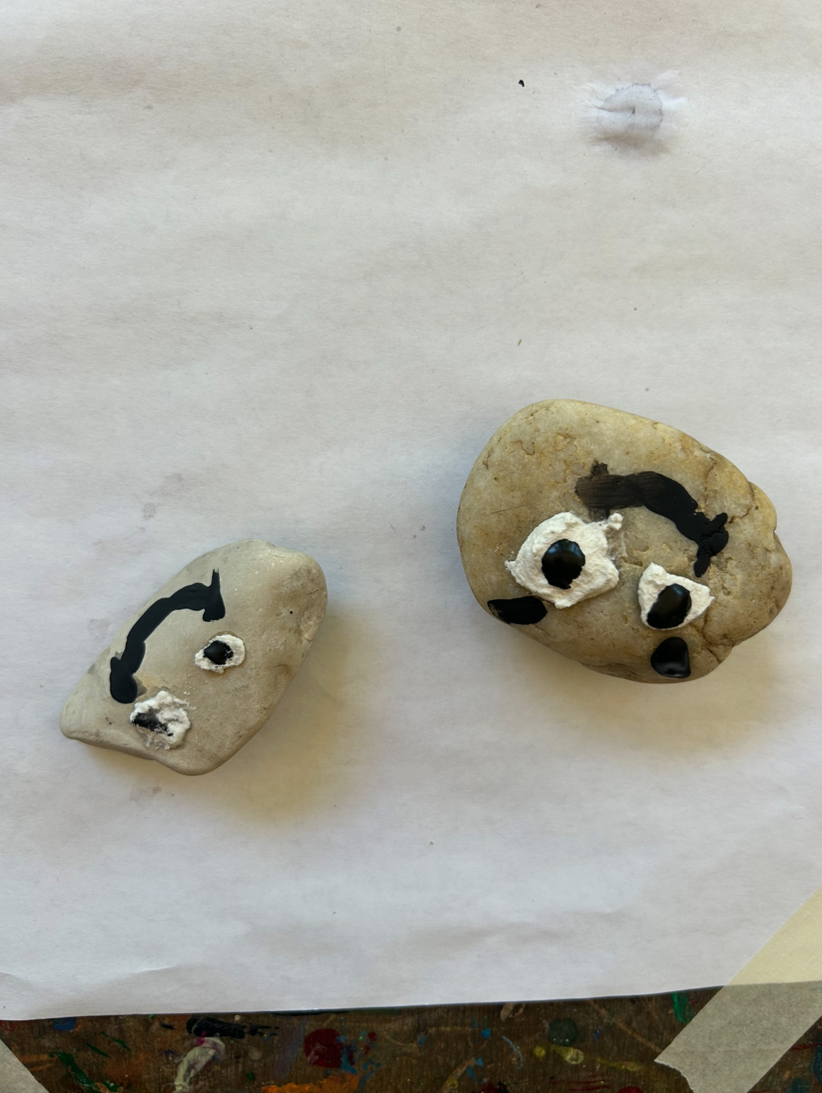 2 bemalte Steine mit Gesichtern liegen auf Papier