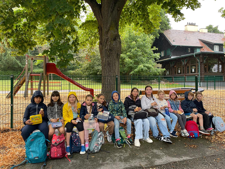Gruppe an Kindern sitzt auf Pank und hält Essen in der Hand
