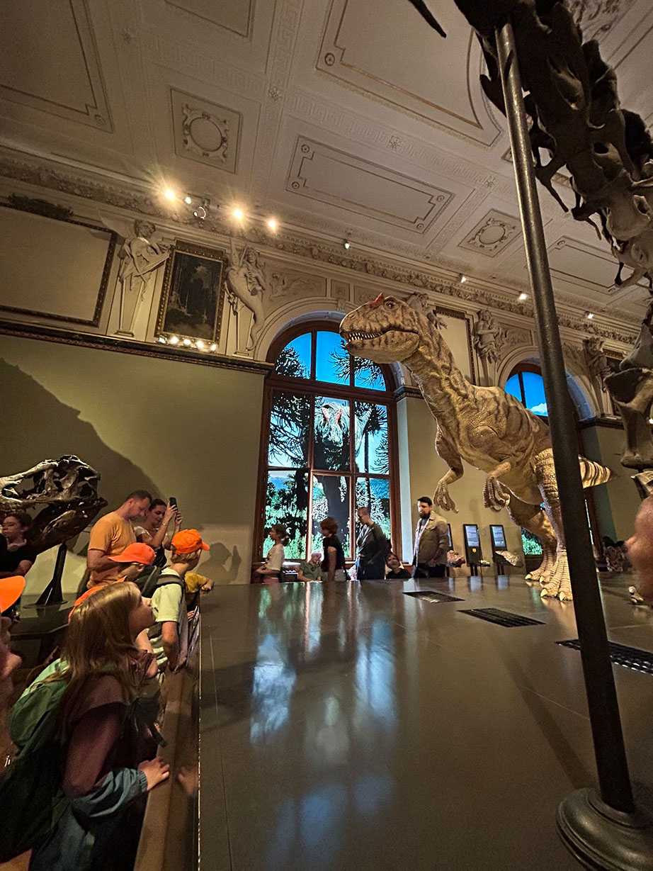 Eine Gruppe an Menschn bestaunt eine Figur eines Dinosauriers